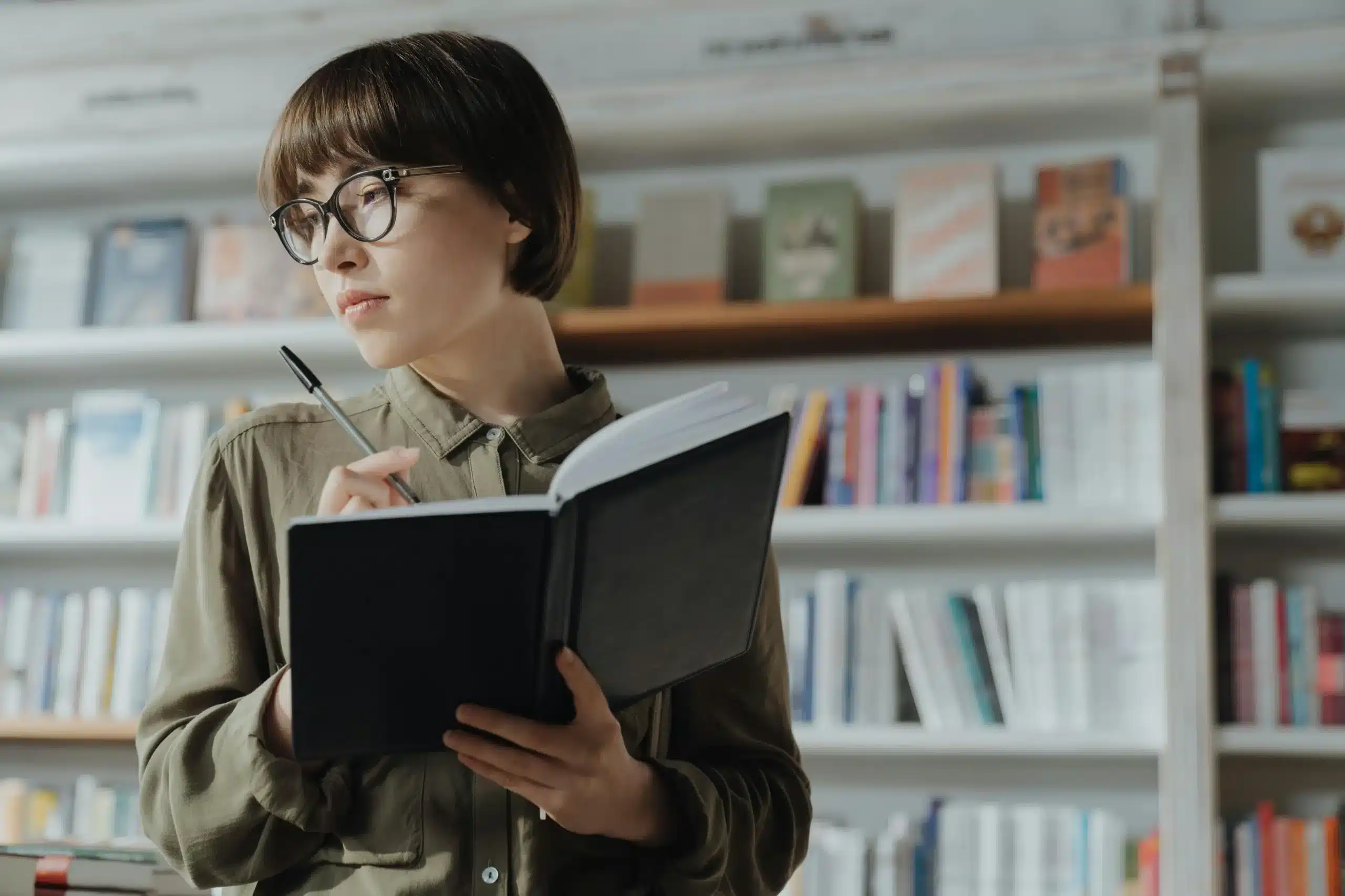 A woman writes in a notebook in front of bookshelves. This focused moment reflects how ketamine for ADHD may help improve attention and clarity.