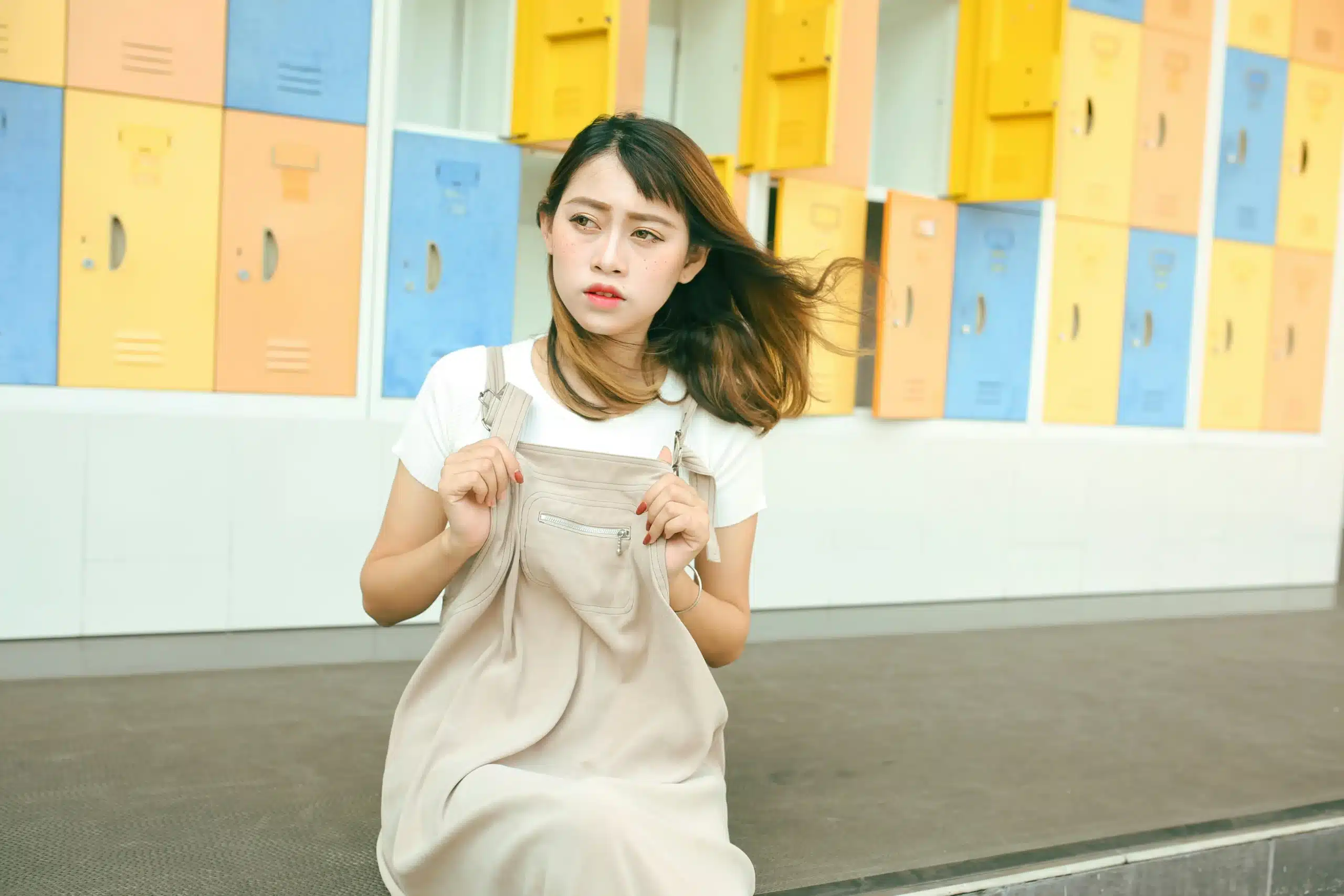A young woman sits alone in front of colorful lockers, looking pensive as the wind blows her hair, reflecting the emotional weight often linked to ketamine for bipolar disorder treatment.