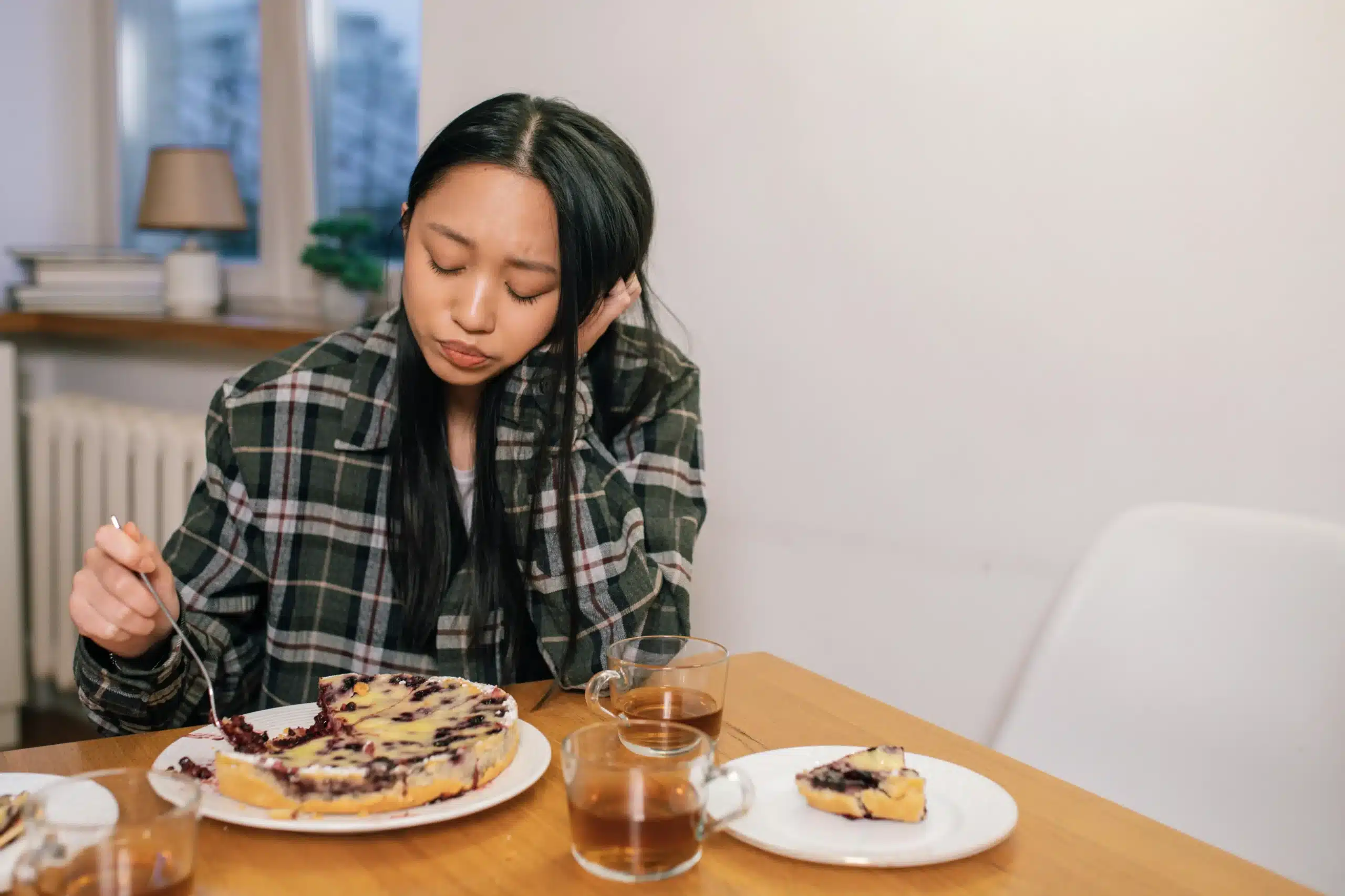 A young woman sits quietly at a table with food, appearing withdrawn. The image reflects the emotional weight tied to meals, often seen in those exploring ketamine for eating disorders.